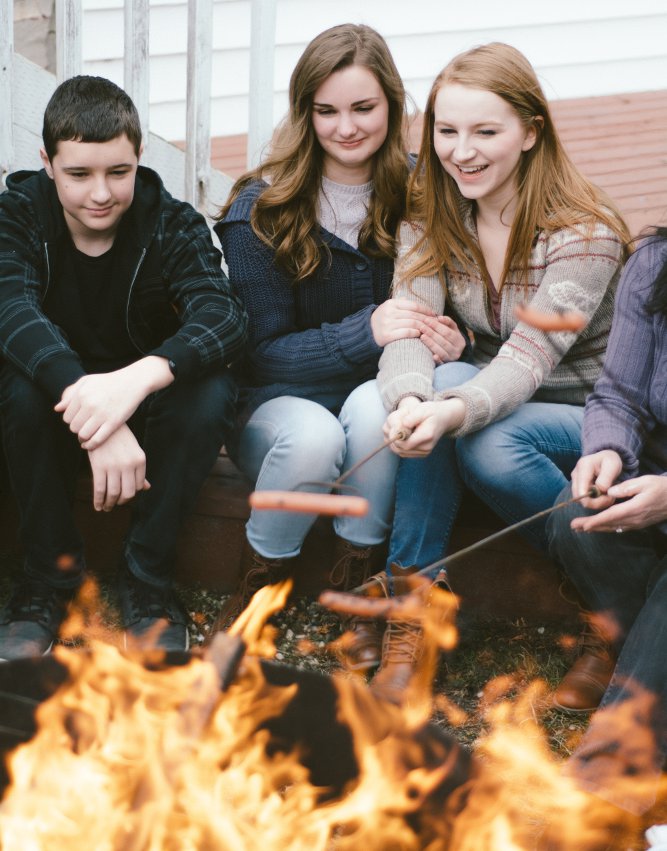 Teenagers roasting hot dogs over the fire